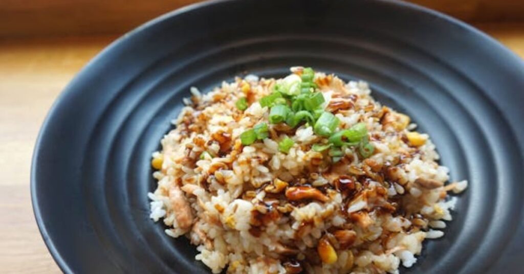 Colorful fried rice with peas, carrots, scrambled egg, and soy sauce in a frying pan